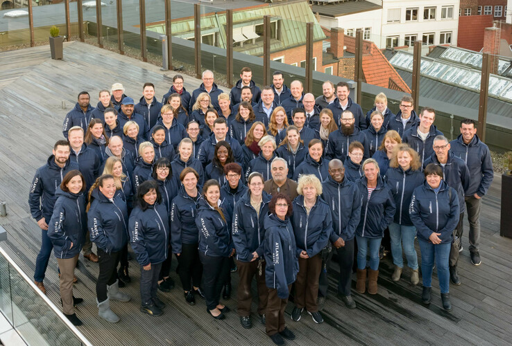 Mitarbeiter ATLANTIC Hotels - 340 Jubilare Große Gruppe von Hotelmitarbeitern in blauen Jacken auf einer Dachterrasse, lächelnd in die Kamera.