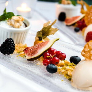 Speisen und Getränke im ATLANTIC Grand Hotel Travemünde Elegantes Dessert mit Feigen, Beeren, Nüssen und Gebäck auf Glasplatte, stimmungsvoll beleuchtet.