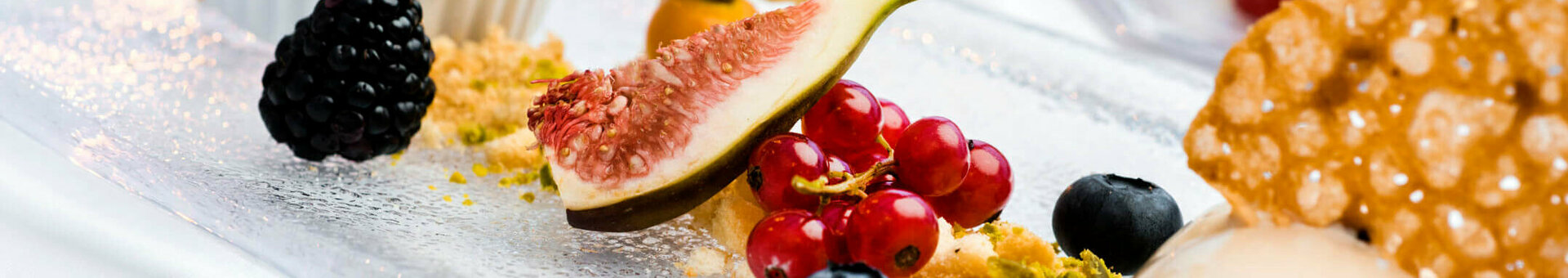 Elegant dessert with figs, berries, nuts and cookies on a glass plate, atmospherically lit.