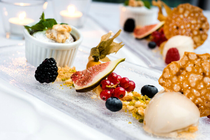 Speisen und Getränke im ATLANTIC Grand Hotel Travemünde Elegantes Dessert mit Feigen, Beeren, Nüssen und Gebäck auf Glasplatte, stimmungsvoll beleuchtet.