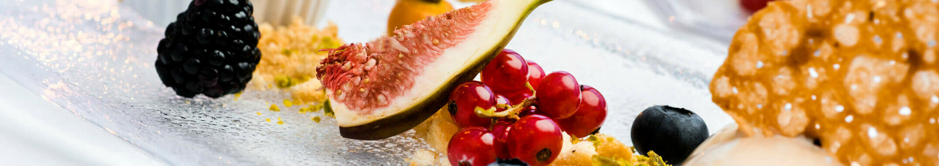 Speisen und Getränke im ATLANTIC Grand Hotel Travemünde Elegantes Dessert mit Feigen, Beeren, Nüssen und Gebäck auf Glasplatte, stimmungsvoll beleuchtet.