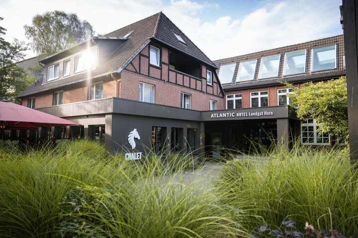 Half-timbered house of the ATLANTIC Hotel Landgut Horn Bremen with green garden in the foreground and sunshine on the roof.