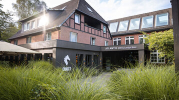 Fachwerkhaus des ATLANTIC Hotel Landgut Horn Bremen mit grünem Garten im Vordergrund und Sonnenschein auf dem Dach.