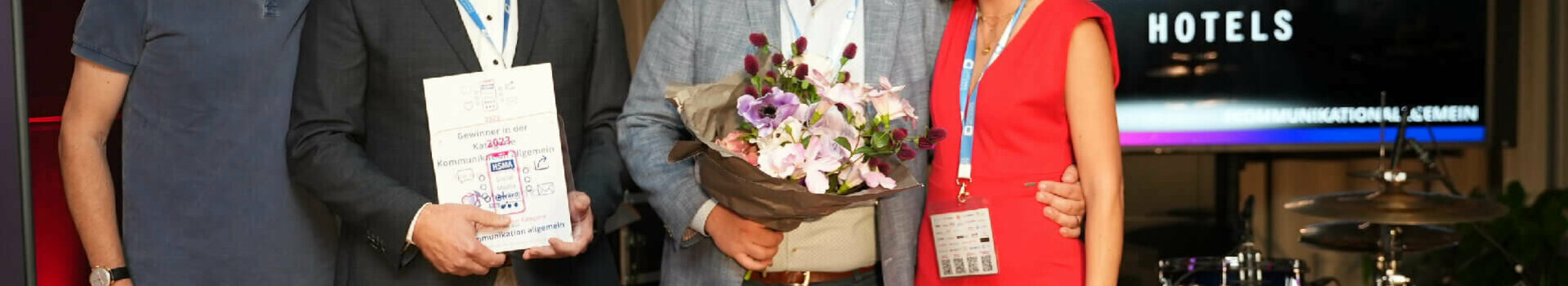 HSMA Social Media Award | ATLANTIC Hotel Sail City Four people at an award ceremony at the ATLANTIC Hotel, one holding flowers, another a certificate.
