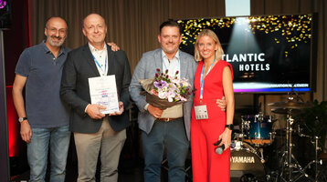 Vier Personen bei einer Preisverleihung im ATLANTIC Hotel, eine hält Blumen, eine andere eine Urkunde.