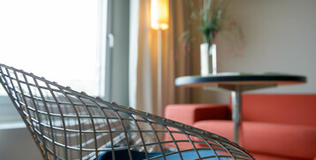 Moderner Hotelraum mit rotem Sofa, Metallstuhl, rundem Tisch und Stehlampe im ATLANTIC Hotel Universum, Bremen.