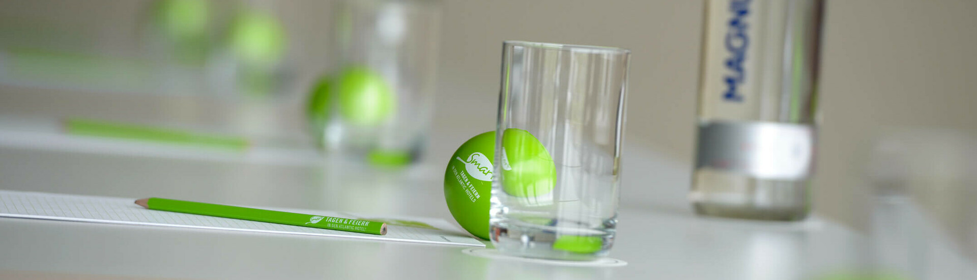 Konferenztisch mit grünen Bällen, Gläsern, Stiften und einer Wasserflasche, stilvoll arrangiert.