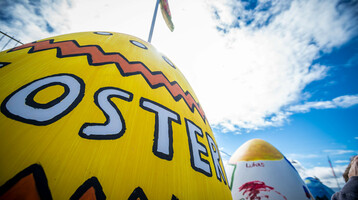 Bunt bemalte Ostereier mit Schriftzug vor blauem Himmel, symbolisieren ein festliches Ereignis.