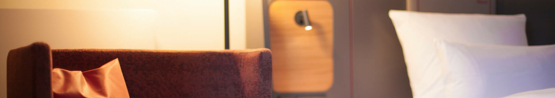 Modernes Hotelzimmer mit gemütlichem Sessel, Nachttischlampe und einem Bett mit weißen Kissen im ATLANTIC Hotel Airport.