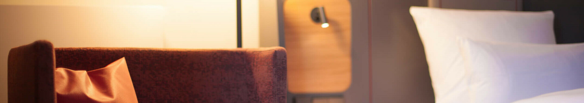 Modern hotel room with cozy armchair, bedside lamp and a bed with white pillows at the ATLANTIC Hotel Airport.