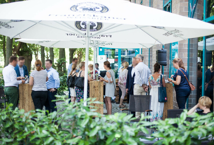 People enjoy an outdoor event under parasols in front of the ATLANTIC Hotel Airport Bremen.