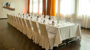 Elegant, festively decorated banquet at the ATLANTIC Hotel Kiel with long tables, white tablecloths and floral decorations.