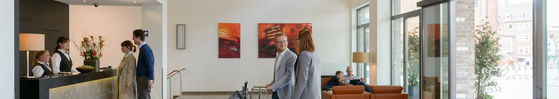 Bright hotel lobby with guests at the reception, modern furniture and large windows at the ATLANTIC Hotel Lübeck.