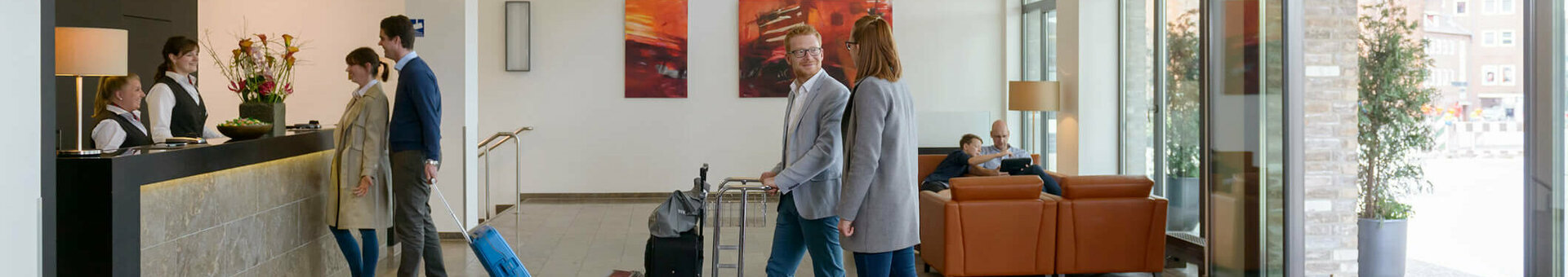 ATLANTIC Hotel Lübeck – Foyer Helle Hotel-Lobby mit Gästen an der Rezeption, modernen Möbeln und großen Fenstern im ATLANTIC Hotel Lübeck.
