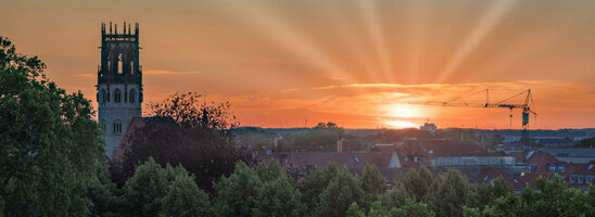 ATLANTIC Hotel Münster Skybar Ausblick Sonnenuntergang über Münster mit Kirchturm, Bäumen und einem Kran im Vordergrund.