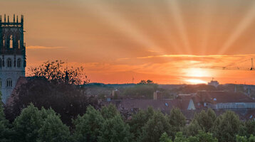 ATLANTIC Hotel Münster Skybar Ausblick Sonnenuntergang über Münster mit Kirchturm, Bäumen und einem Kran im Vordergrund.