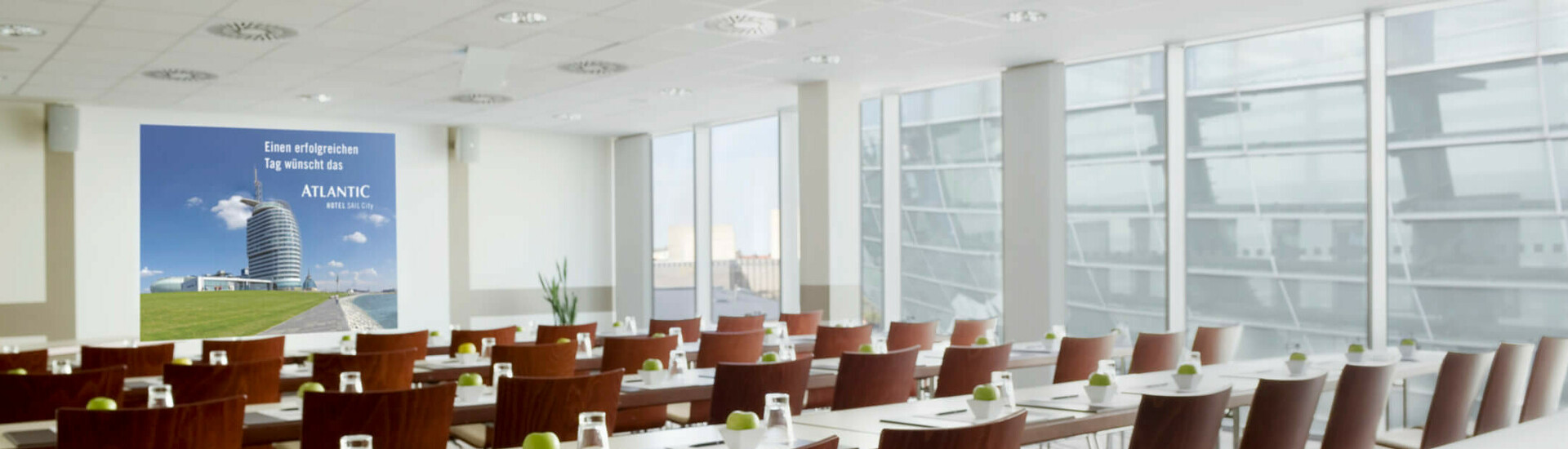 Moderner Konferenzraum im ATLANTIC Hotel Sail City, Bremerhaven, mit Tischen, Stühlen, Schreibutensilien und grünen Äpfeln.