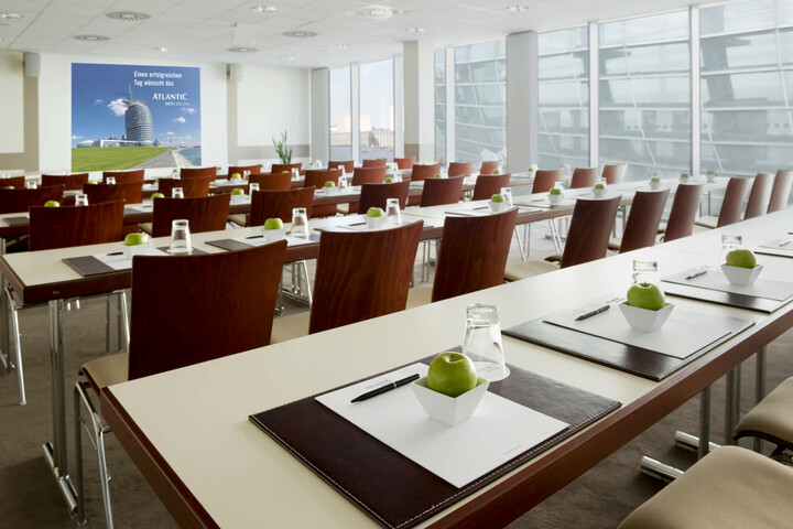 Modern conference room in the ATLANTIC Hotel Sail City, Bremerhaven, with tables, chairs, writing utensils and green apples.