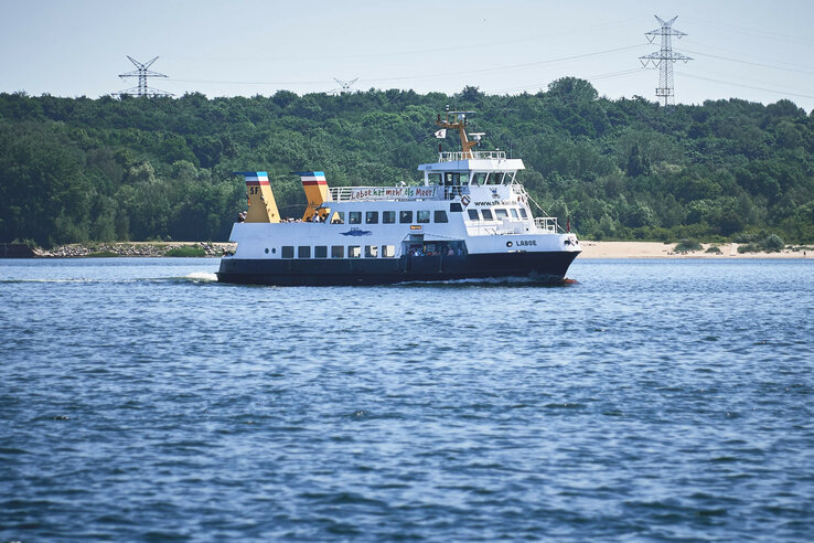Eine Fähre fährt auf dem Wasser vor einer bewaldeten Küste entlang.