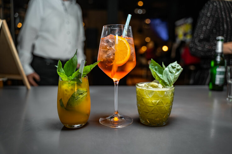 Three colorful cocktails on a bar in the ATLANTIC Grand Hotel Bremen, decorated with fresh herbs and fruits.
