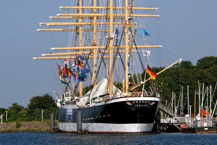 Großes Segelschiff "Passat" im Hafen von Travemünde, umgeben von bunten Flaggen und ruhigem Wasser.