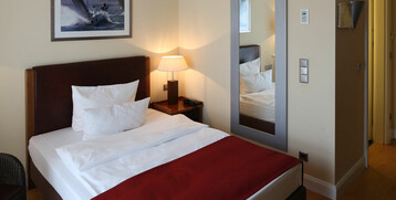 Gemütliches Hotelzimmer mit Doppelbett, roter Decke, Nachttischlampe und großem Wandspiegel.