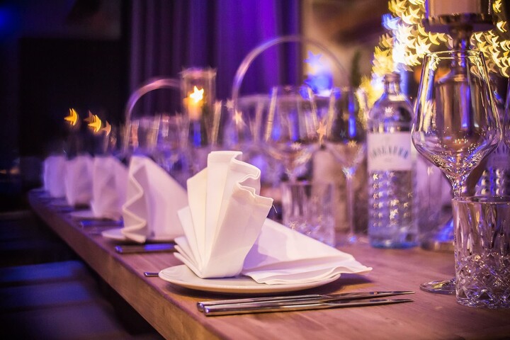 Eleganter, festlich gedeckter Tisch mit gefalteten Servietten, Gläsern und Kerzen in stimmungsvoller Beleuchtung.