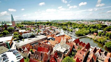 Blick auf Lübecks Altstadt mit roten Ziegeldächern, Kirchtürmen und Fluss bei klarem Himmel.