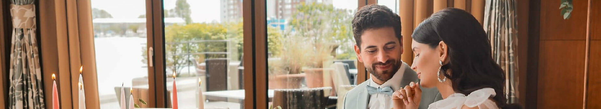 Ein elegantes Paar sitzt an einem festlich gedeckten Tisch mit Blumen und Kerzen im ATLANTIC Hotel Wilhelmshaven.