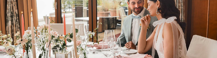 An elegant couple sits at a festively laid table with flowers and candles in the ATLANTIC Hotel Wilhelmshaven.