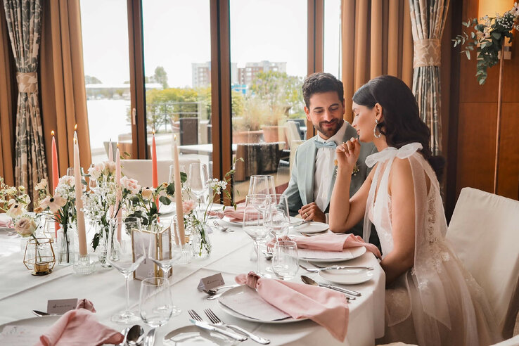An elegant couple sits at a festively laid table with flowers and candles in the ATLANTIC Hotel Wilhelmshaven.