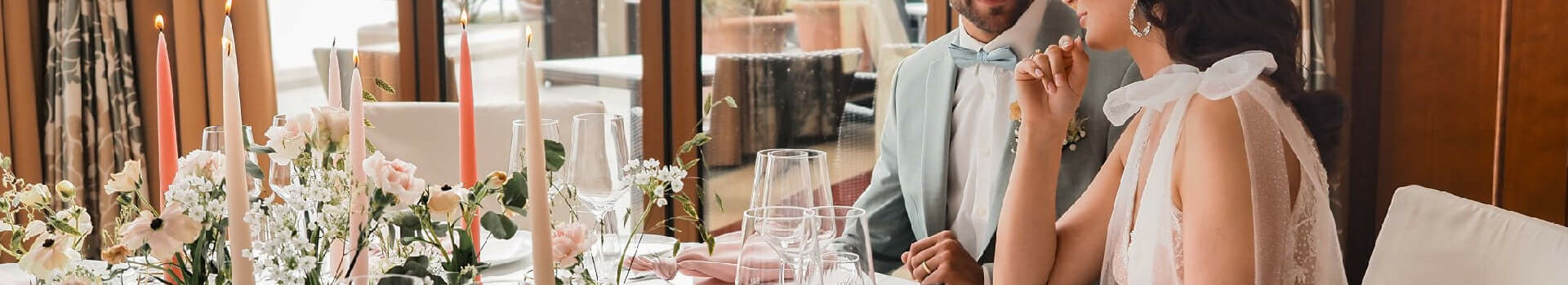 An elegant couple sits at a festively laid table with flowers and candles in the ATLANTIC Hotel Wilhelmshaven.