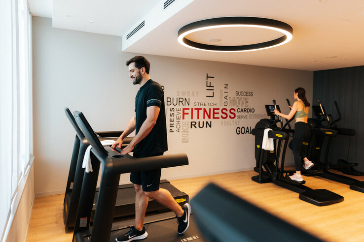 Fitness room in the ATLANTIC Hotel Heidelberg with two people on treadmills in front of a wall with motivational words.