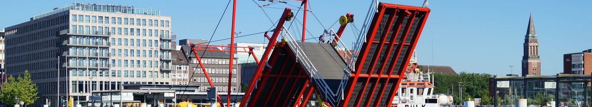 ATLANTIC Hotel Kiel | Deal Off to the real north Red bascule bridge over water, modern buildings and church tower in the background under a clear sky.
