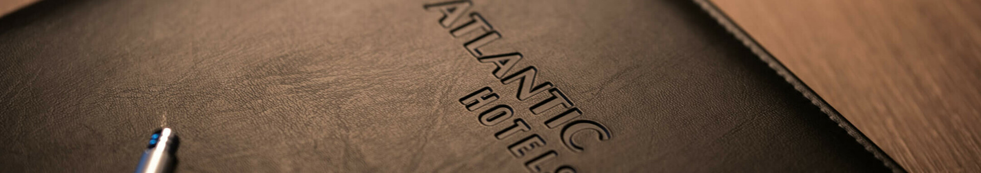 Schwarze Ledermappe mit "ATLANTIC HOTELS"-Prägung auf Holztisch, daneben ein silberner Kugelschreiber.