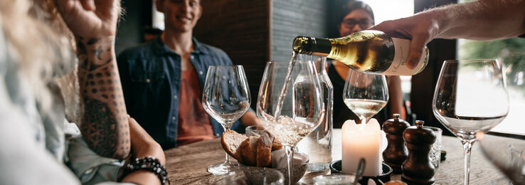 Gemütliche Runde im ATLANTIC Hotel Münster: Wein wird eingeschenkt, Kerzenlicht, Brot und Vorspeisen auf dem Tisch.
