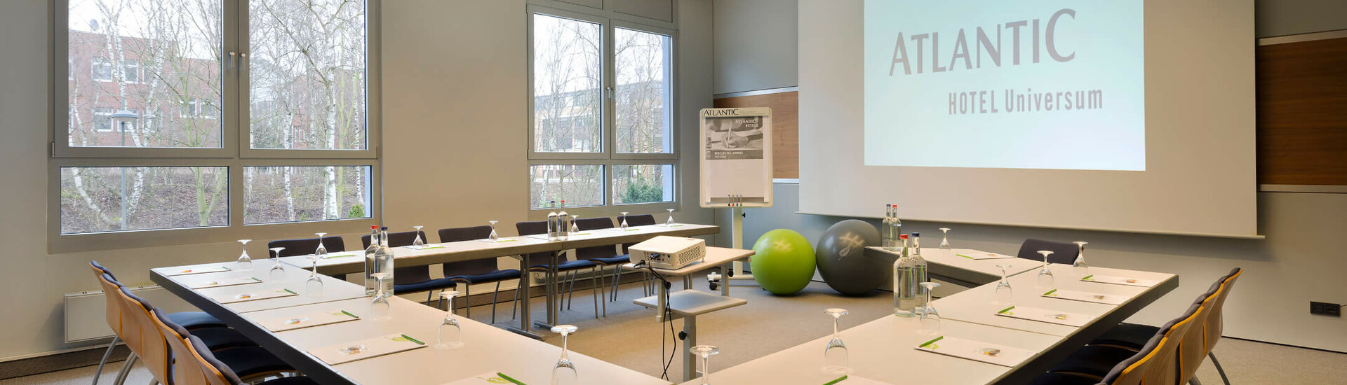 ATLANTIC Hotel Universum – Tagungsraum Albert Einstein Konferenzraum im ATLANTIC Hotel Universum mit U-förmiger Tischanordnung, Leinwand und Flipchart.