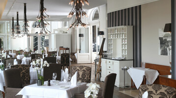 Elegant hotel restaurant with stylishly laid tables, modern chandeliers and floral decorations.