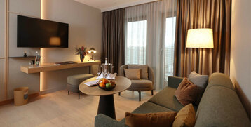 Wohnbereich mit Couch, Tisch und Sessel, Fernseher und Schreibtisch in der Suite im ATLANTIC Hotel Heidelberg 
