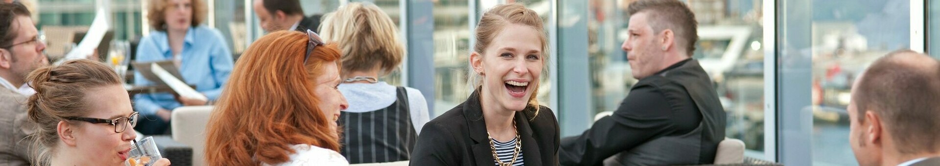 Personen genießen Getränke auf einer modernen Hotel-Dachterrasse mit Blick auf die Stadt.