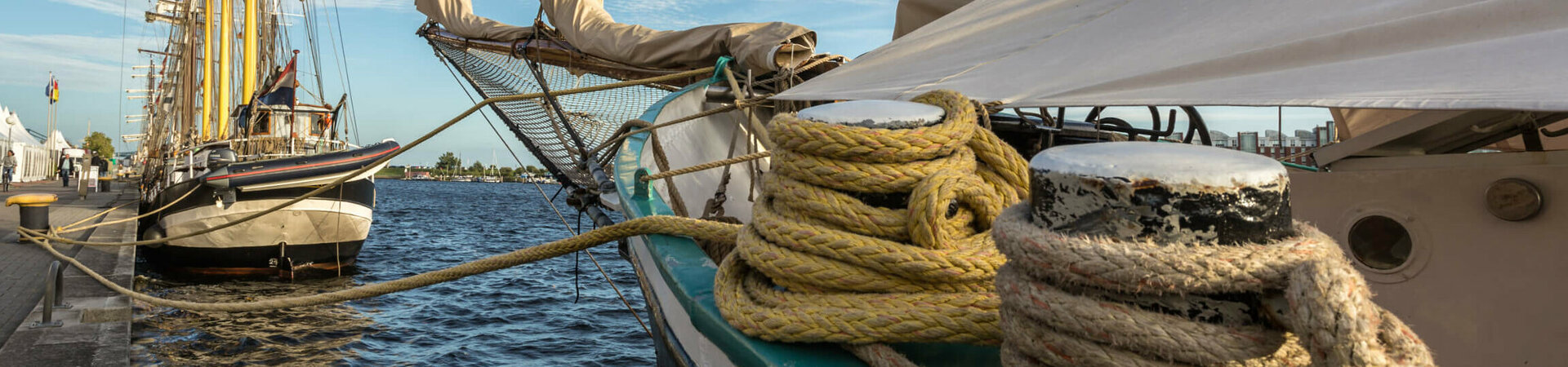 Sailing ships in the harbor, with moored ropes and blue sky in the background.
