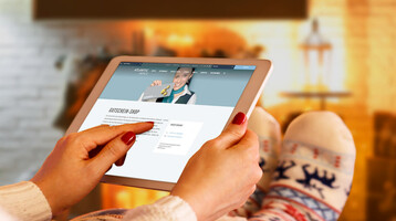 Person relaxing in front of the fireplace with a tablet on which a hotel website is open. Room decorated for Christmas.