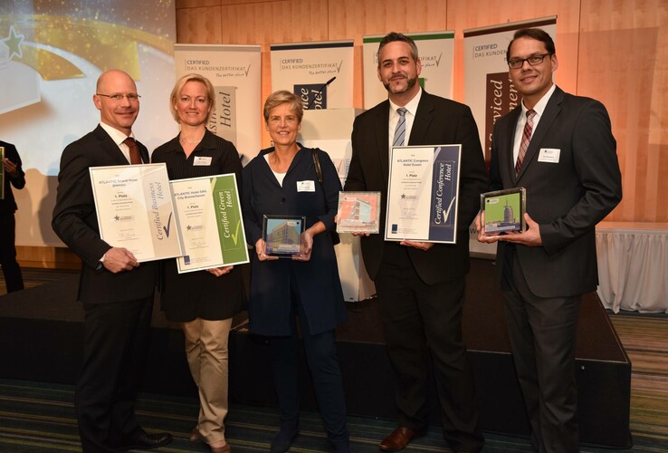 Eine Gruppe von fünf Menschen hält Zertifikate und Auszeichnungen in einem Konferenzraum.