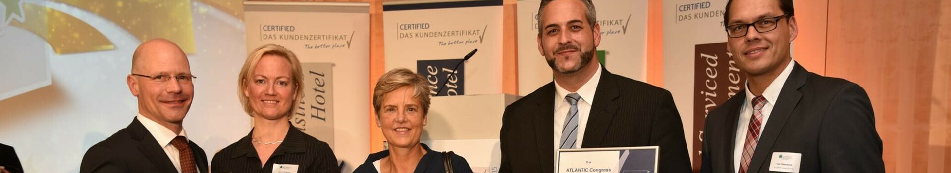 Eine Gruppe von fünf Menschen hält Zertifikate und Auszeichnungen in einem Konferenzraum.