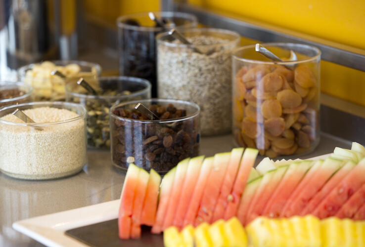 Breakfast buffet with sliced watermelon and pineapple, next to bowls of dried fruit and nuts.