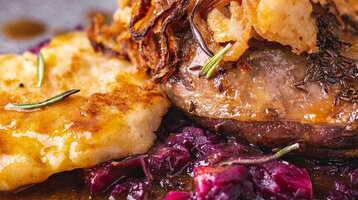 Nahaufnahme eines Stücks Gänsebraten mit Rotkohl und Sauce auf einem dunklen Teller