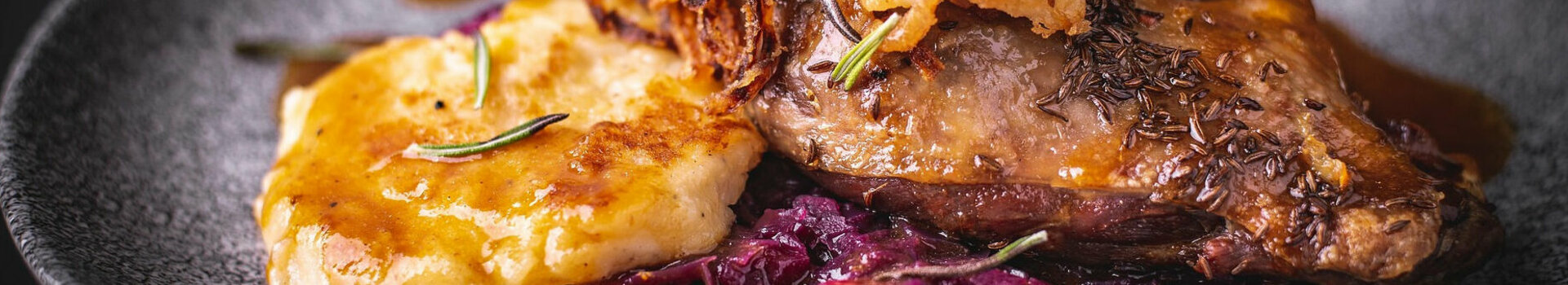 Nahaufnahme eines Stücks Gänsebraten mit Rotkohl und Sauce auf einem dunklen Teller