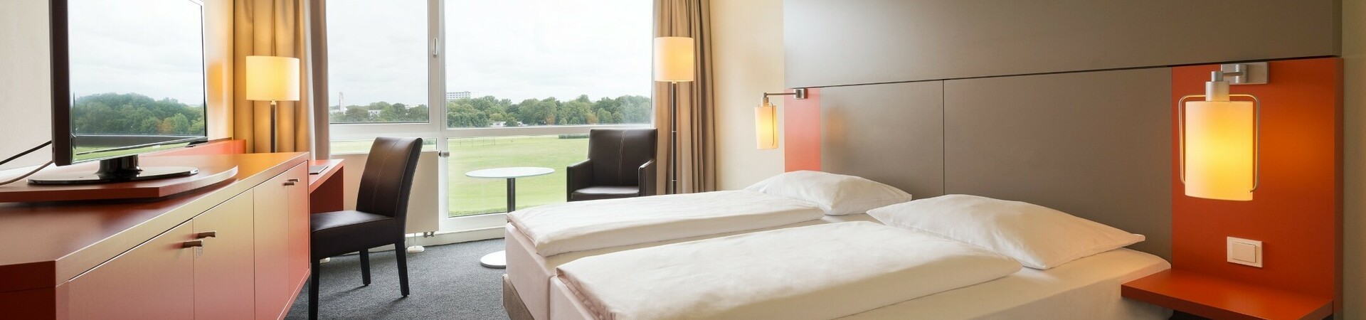 Double Room with a view over the racecourse in the ATLANTIC Hotel Galopprennbahn Bremen Modern hotel room with double bed, large window, TV and view of a green landscape.