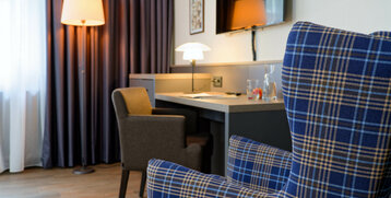 Gemütliches Hotelzimmer mit Schreibtisch, Sessel und Stehlampe, warm beleuchtet, im ATLANTIC Hotel Landgut Horn Bremen.