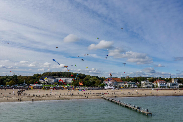 Strand mit vielen Drachen in der Luft, Menschen spazieren, ATLANTIC Grand Hotel Travemünde im Hintergrund.